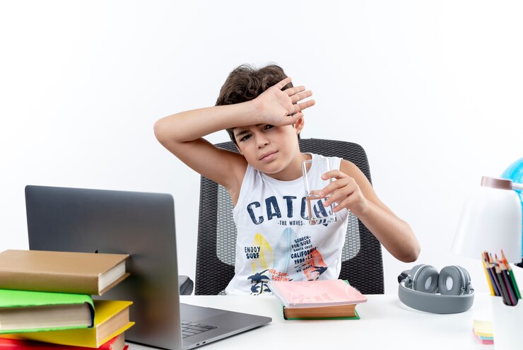 looking-camera-little-schoolboy-sitting-desk-with-school-tools-holding-glass-water-covered-forehead-with-wrist-isolated-white-background_141793-63638