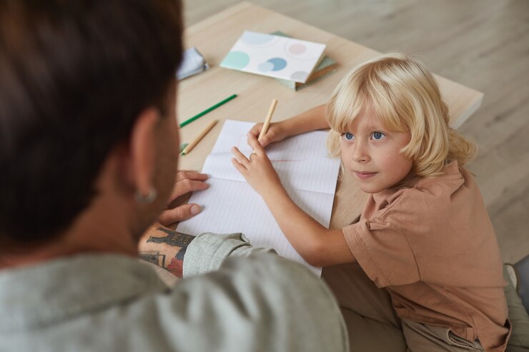 little-son-with-blond-hair-talking-his-father-while-sitting-table-drawing_249974-7174
