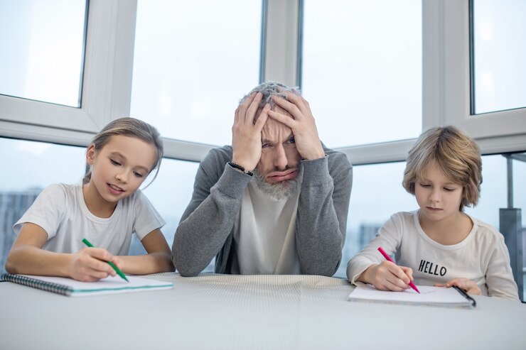 homework-gray-haired-bearded-man-sitting-with-his-kids-table-while-they-doing-lessons_259150-48422