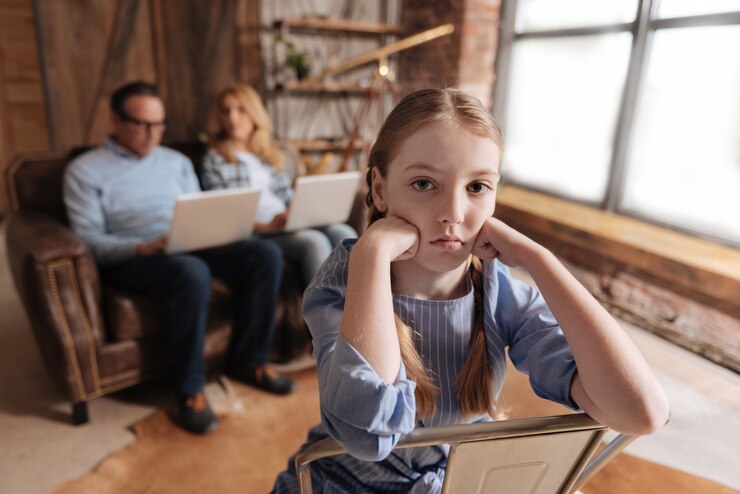 involved-depressed-little-kid-waiting-parents-care-home-feeling-bored-while-father-mother-working-with-laptops_259150-18350